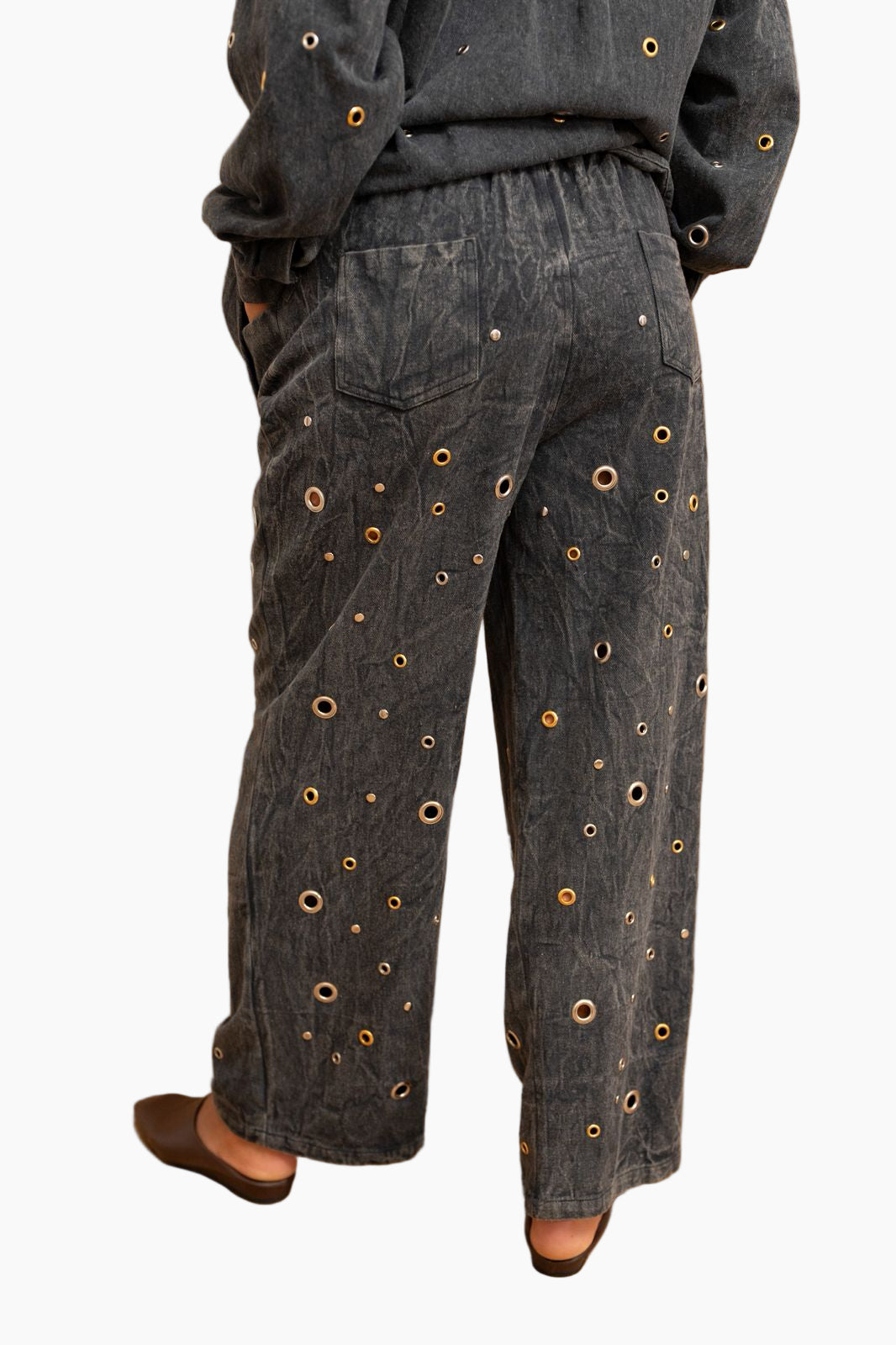 Dark denim pants with eyelet details worn by a person