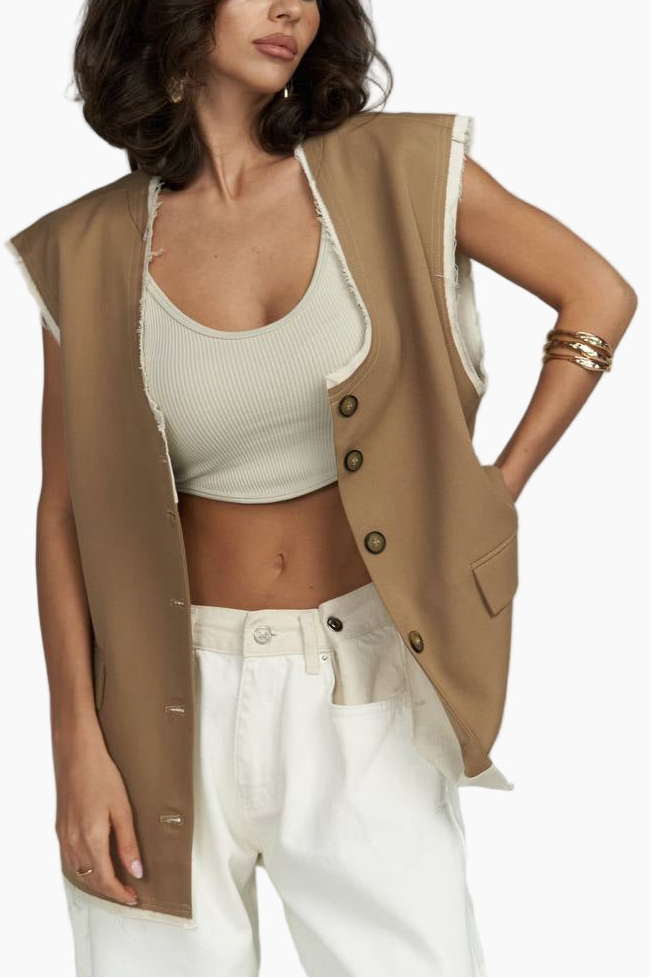 Woman wearing a beige vest over a white top and pants on a plain background
