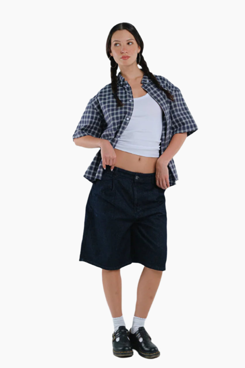 Woman wearing a plaid shirt, white tank top, black shorts, and black shoes