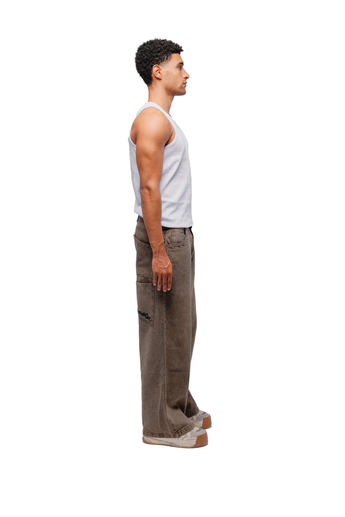 A person standing against a white background, wearing a white tank top and brown baggy pants with multiple pockets.
