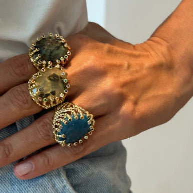 Close-up of a hand wearing two gold rings with gemstones on a neutral background