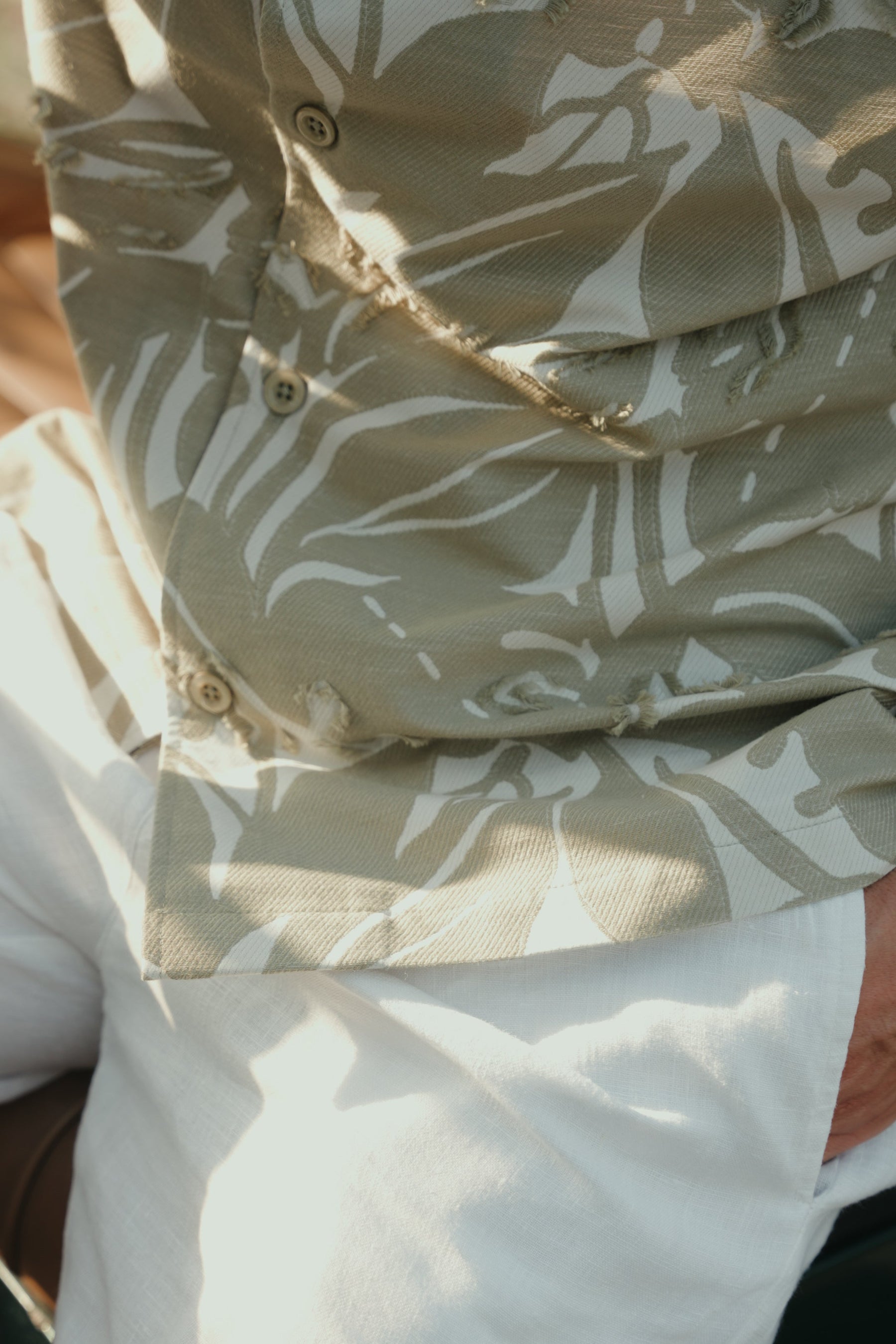 Close-up of a person wearing a beige shirt with white floral pattern and light-colored pants.