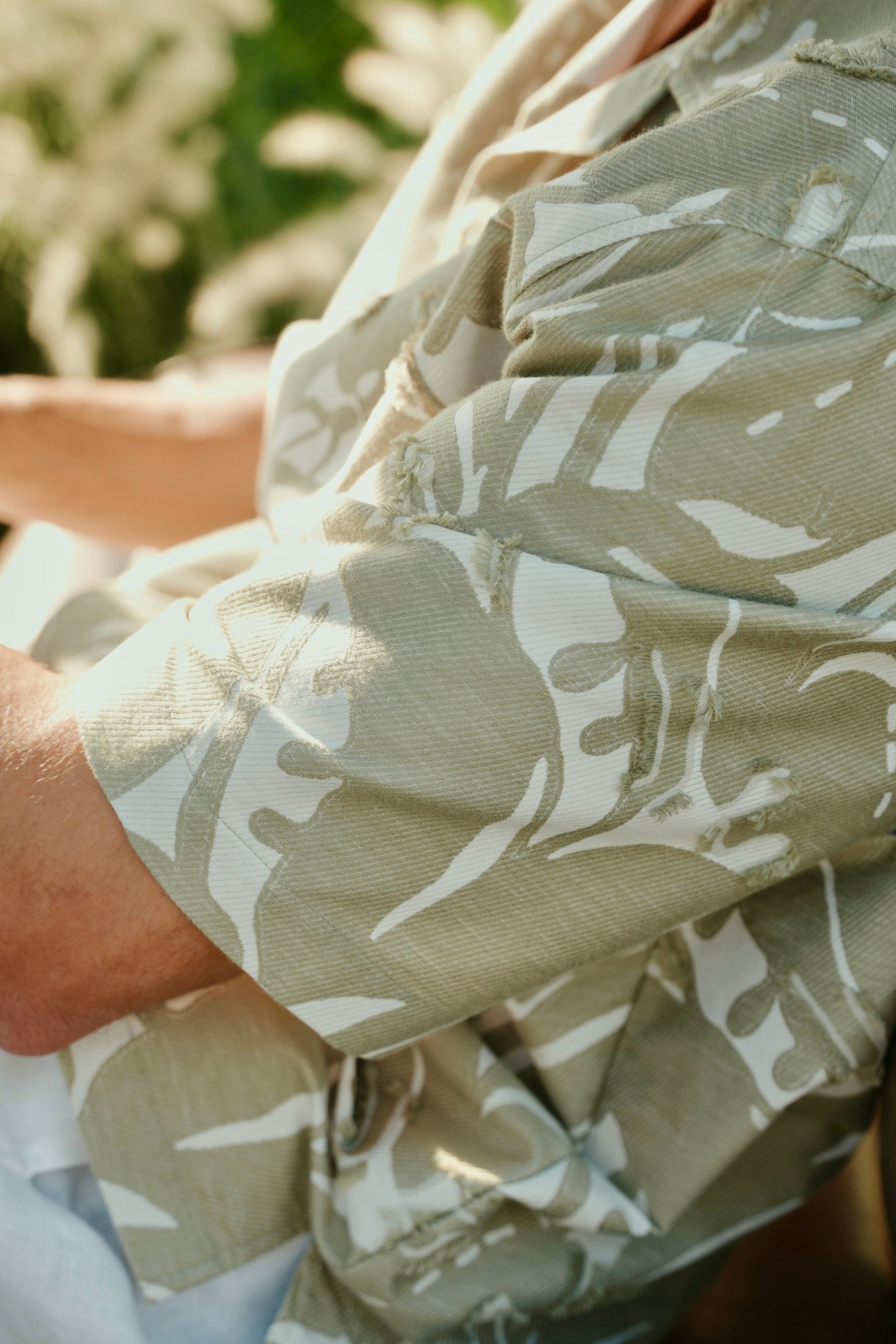 Person wearing a light-colored shirt with a subtle pattern, sitting outdoors.