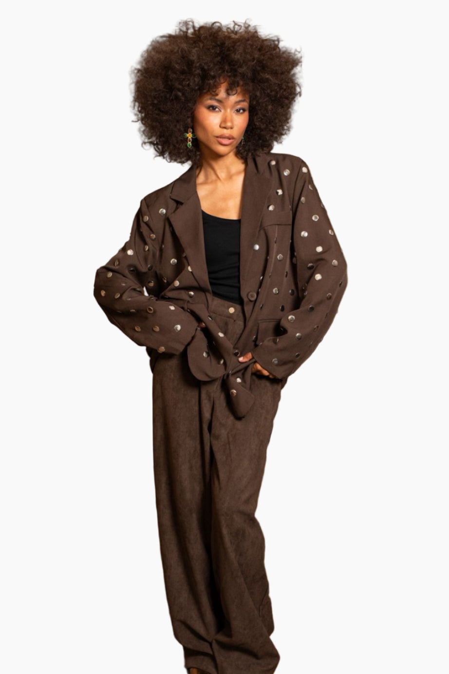 Woman in a brown polka dot suit standing in a room with wooden beams and a staircase.
