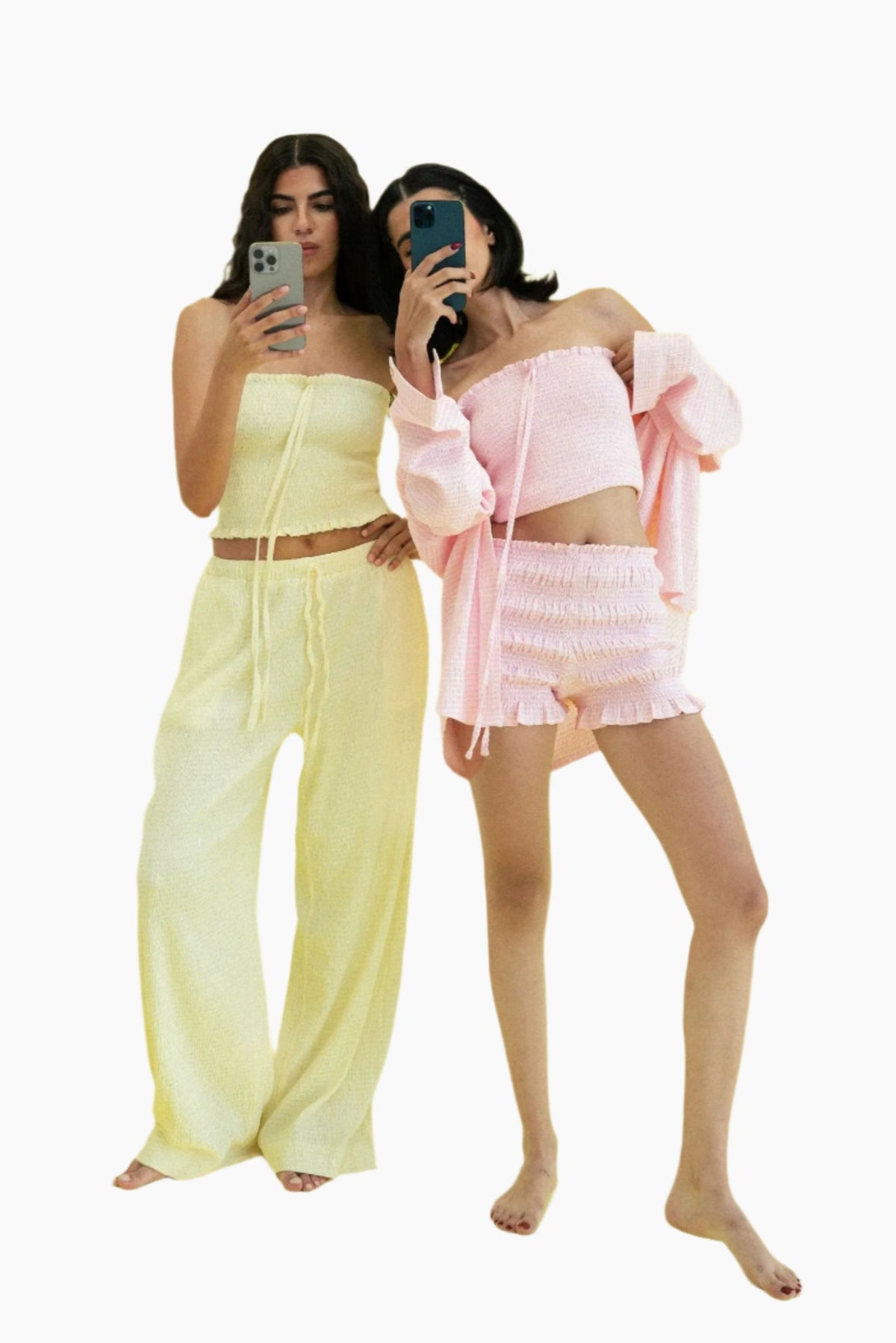Two women taking mirror selfies wearing pastel outfits.