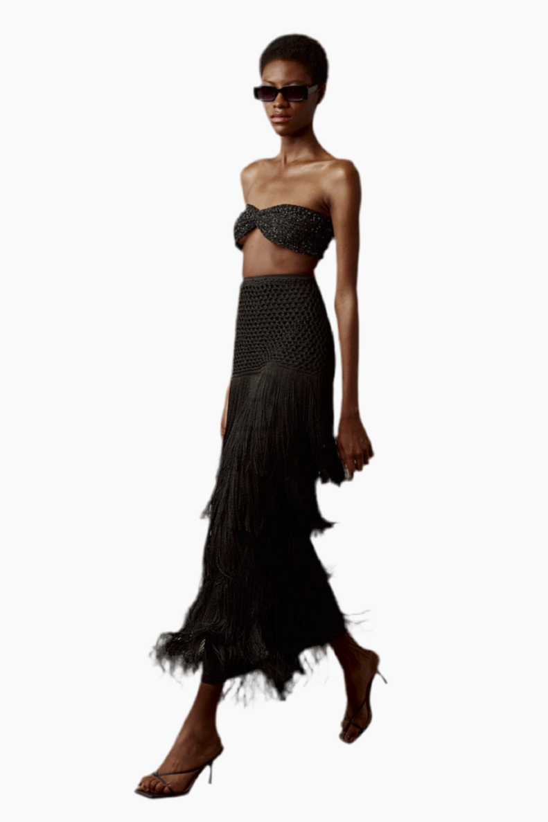 Model wearing a black strapless top and long black skirt with fringe