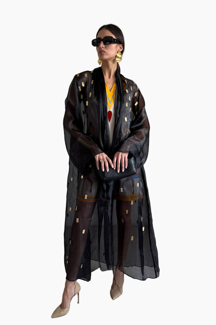Woman wearing a black abaya with gold patterns on a white background