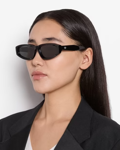 Woman wearing black sunglasses and a black blazer against a white background
