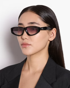 Woman wearing black sunglasses and a black blazer against a white background