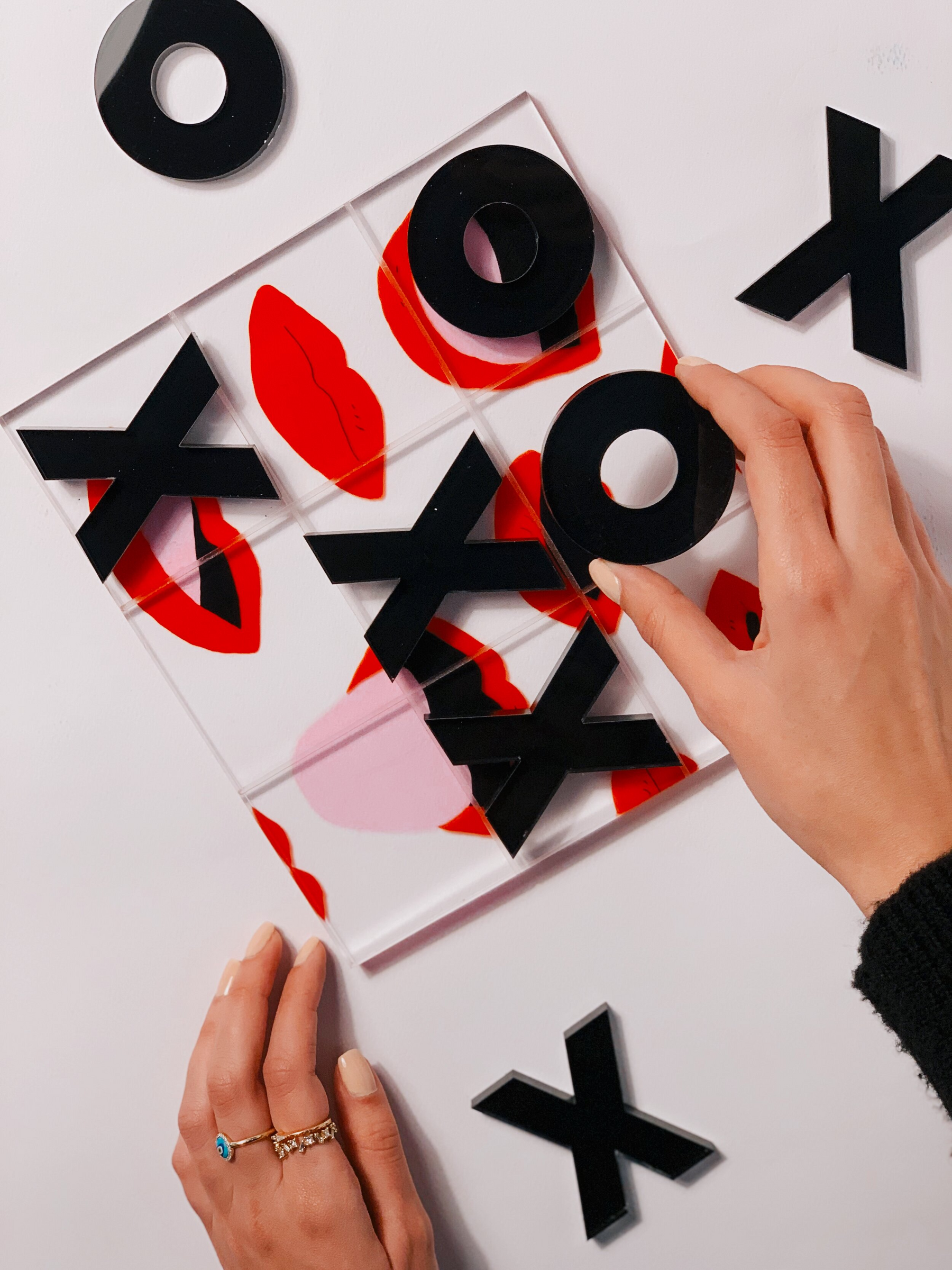 A person's hands placing pieces on a tic tac toe acrylic board, which has a red and black color scheme.