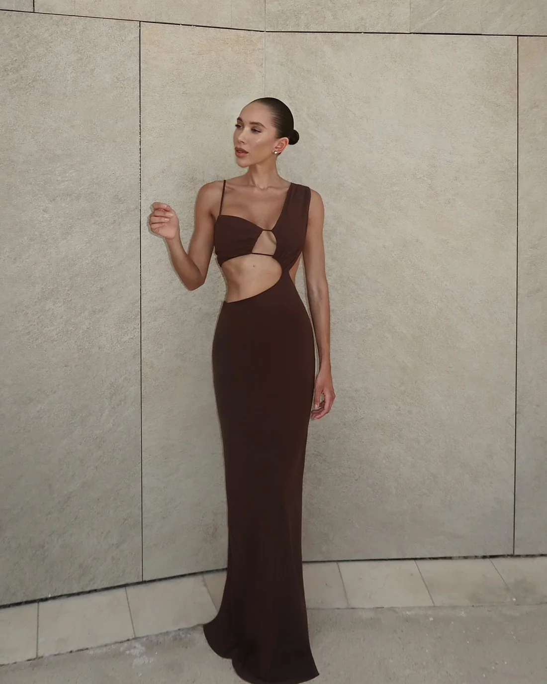 A woman in a chocolate brown maxi dress with a deep neckline and side split.