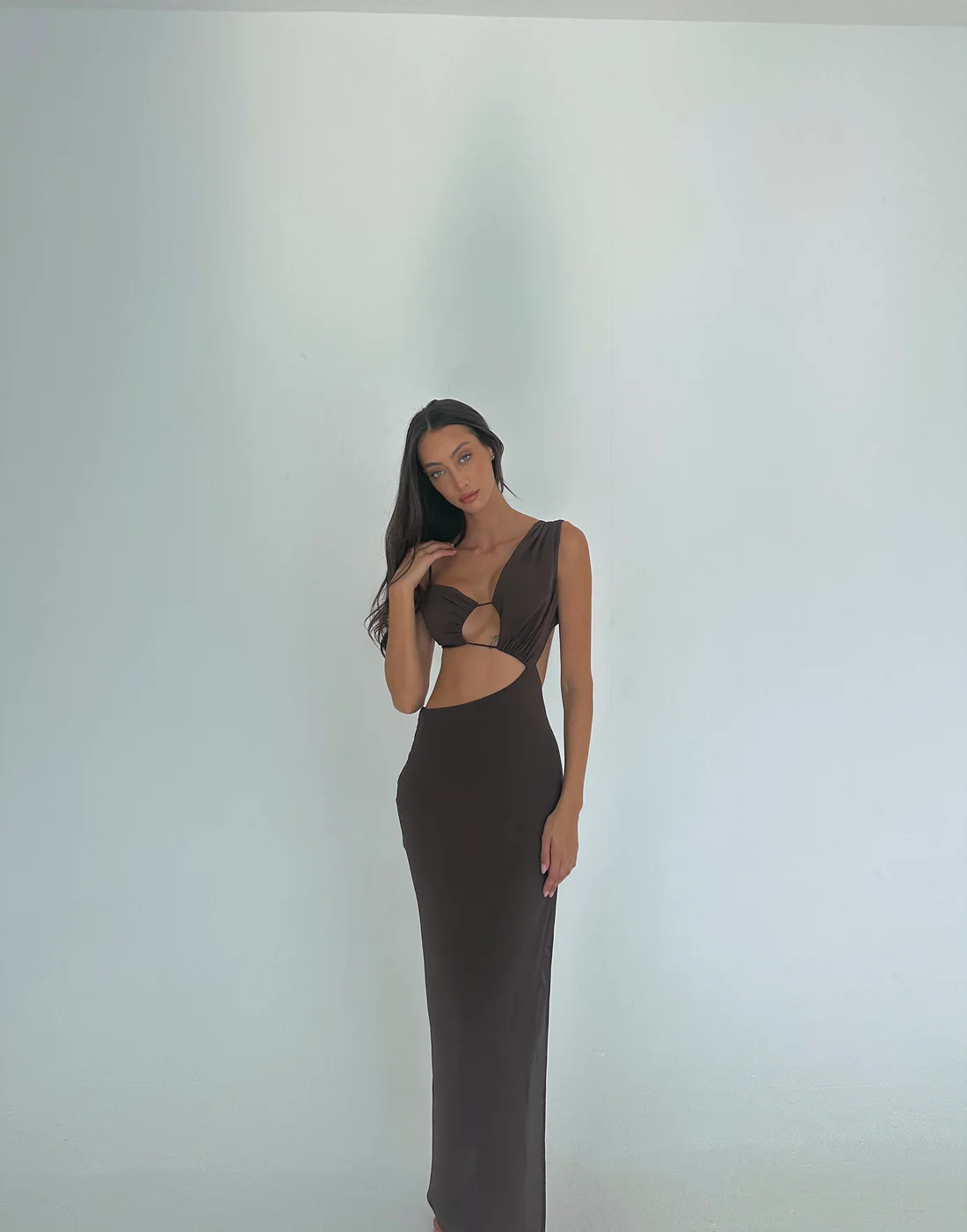 A woman in a chocolate brown maxi dress with a deep neckline and side split.