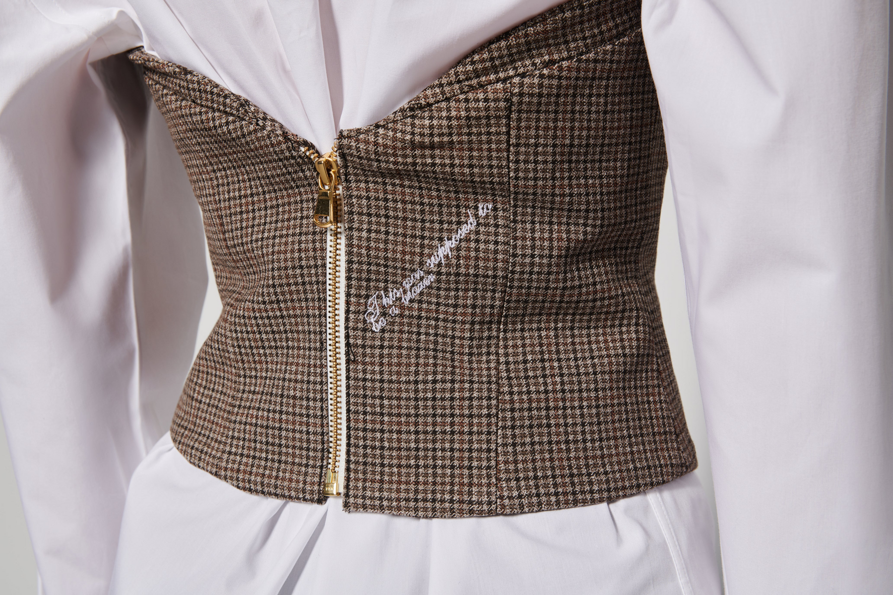 close up A model wearing a brown checkered bustier with collar details and golden buttons, on top of a white chemise dress