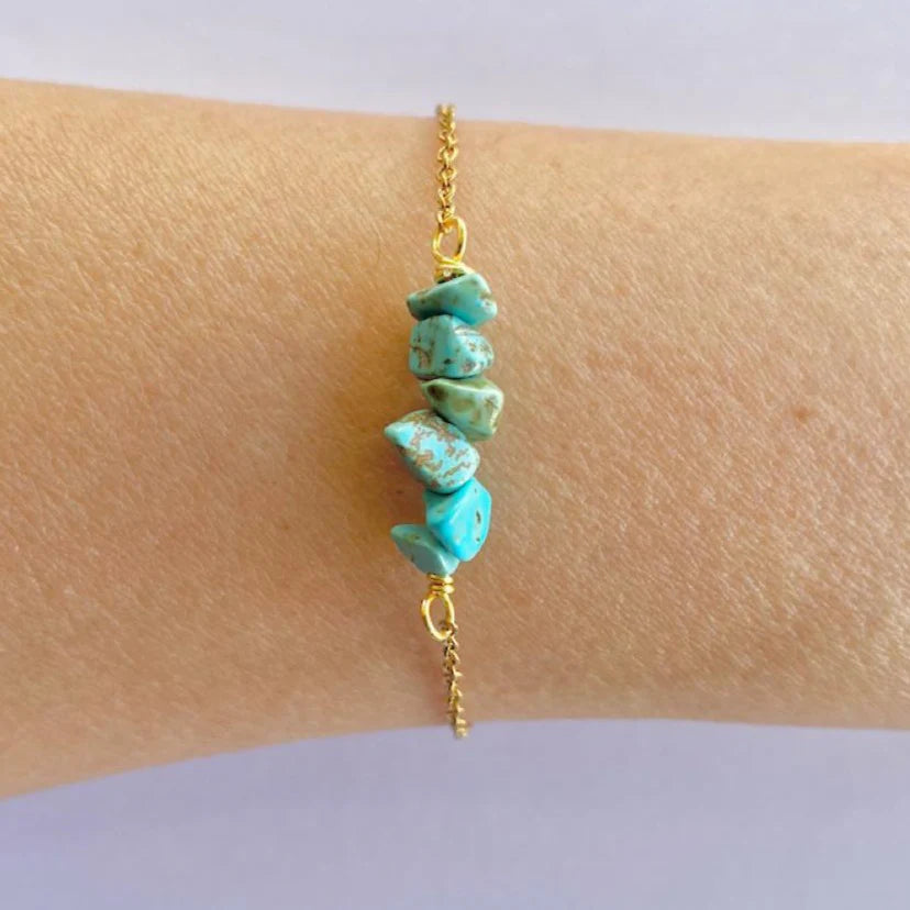 A bracelet with polished natural stones on a gold-colored stainless steel band, being worn on a person's wrist.