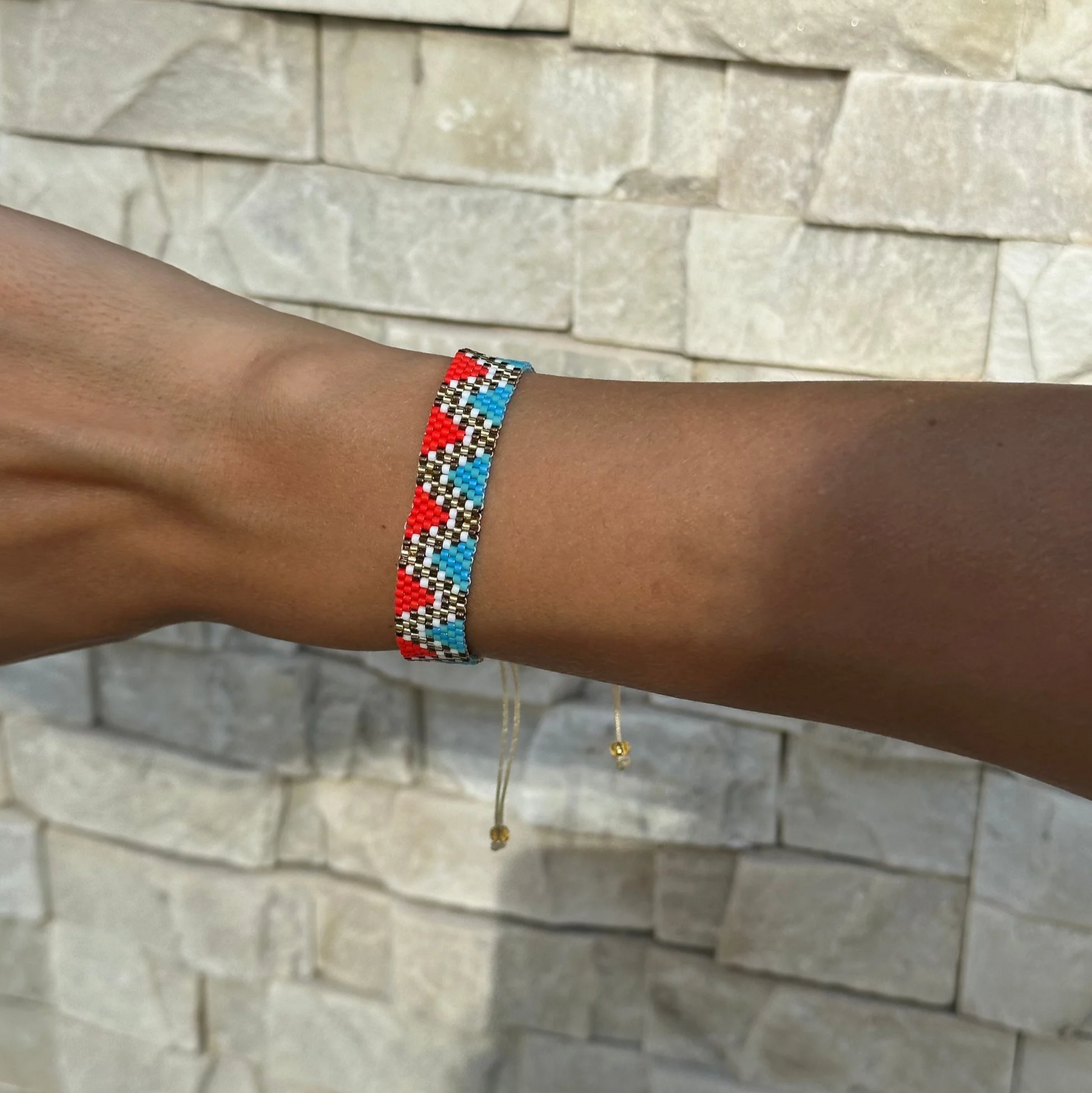 Bracelet with red, blue, and white beads on a wrist against a stone wall background