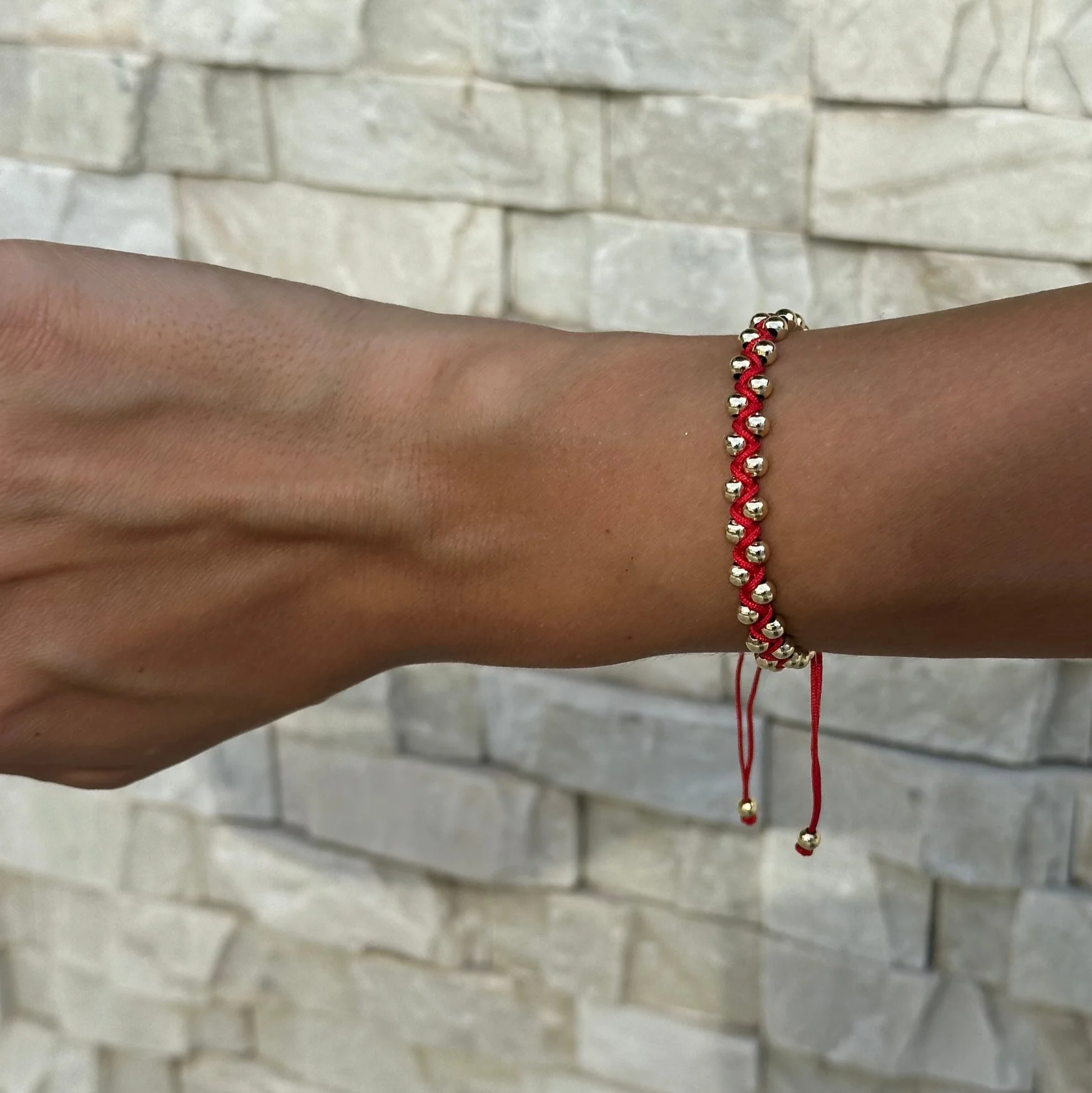 Red beaded bracelet on a wrist against a stone wall background