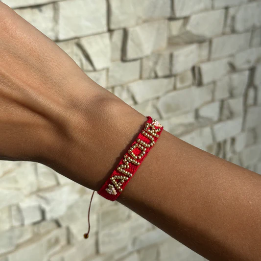 Red and gold bracelet on a wrist with a stone wall background