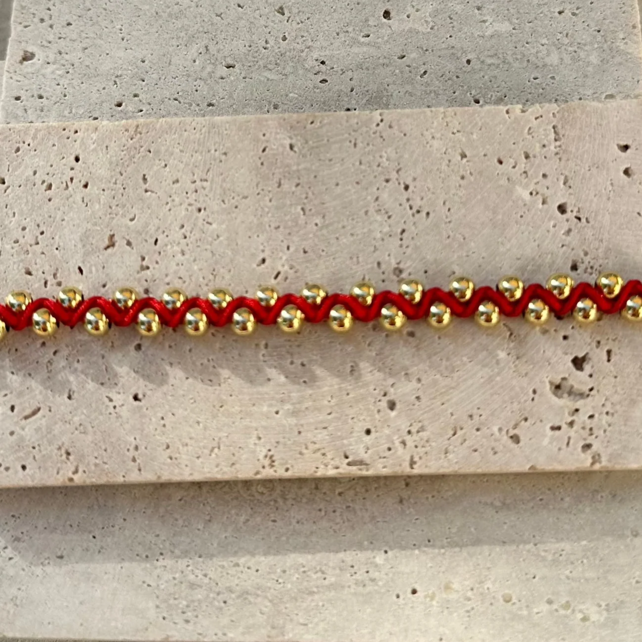 Bracelet with red and gold beads on a stone surface