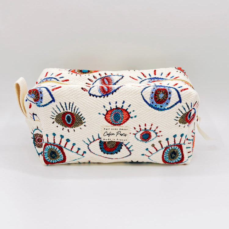 A multicolored cosmetic and toiletry bag with a geometric pattern featuring eye motifs on a white background, with a small handle and decorative elements.
