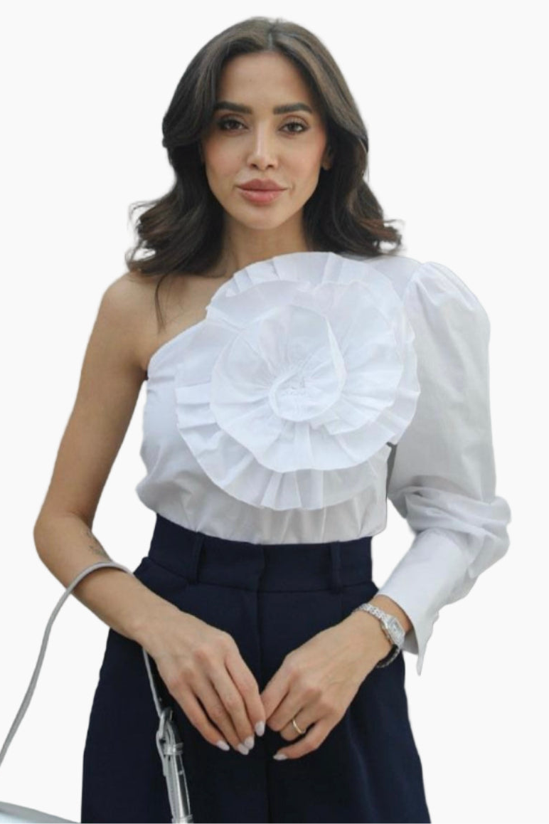 Woman wearing a white one-shoulder ruffled blouse and dark pants on a white background