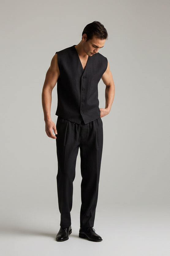 Man wearing a black sleeveless vest and pants on a plain background