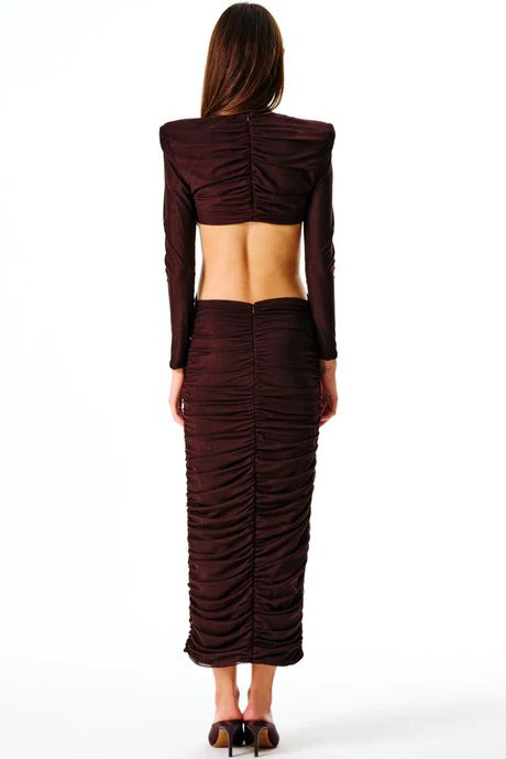 A woman standing and facing to the side wearing a brown maxi dress with a cut-out back and a decorative belt.