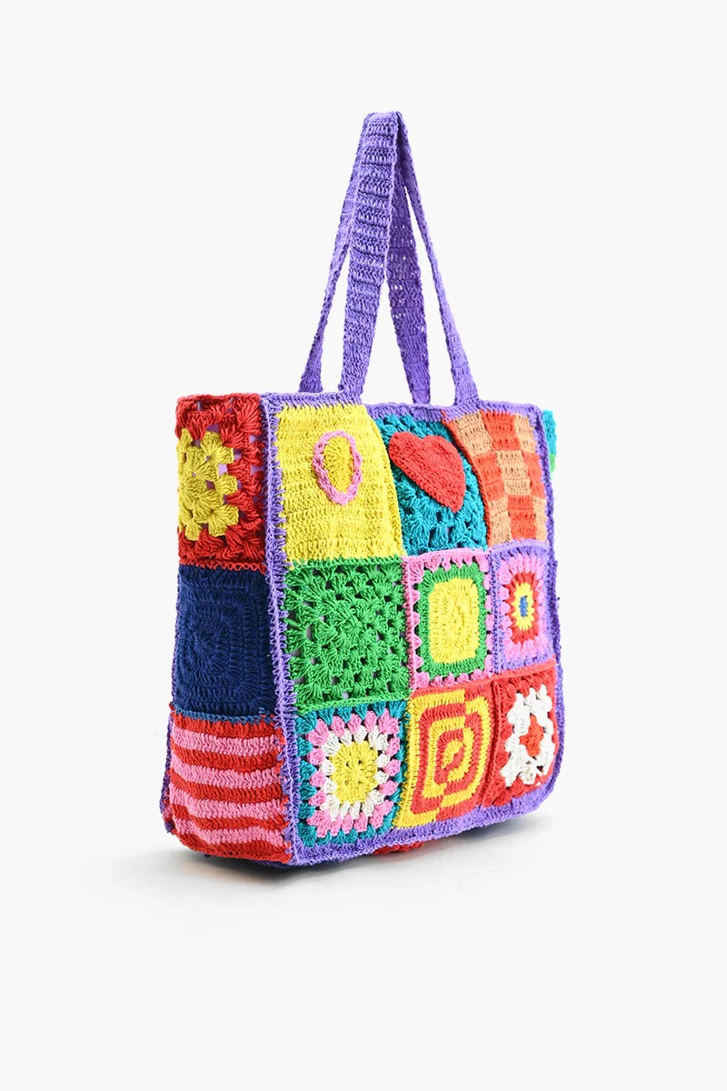A multicolored crochet tote bag with a playful, patchwork design featuring various geometric and heart-shaped patterns.