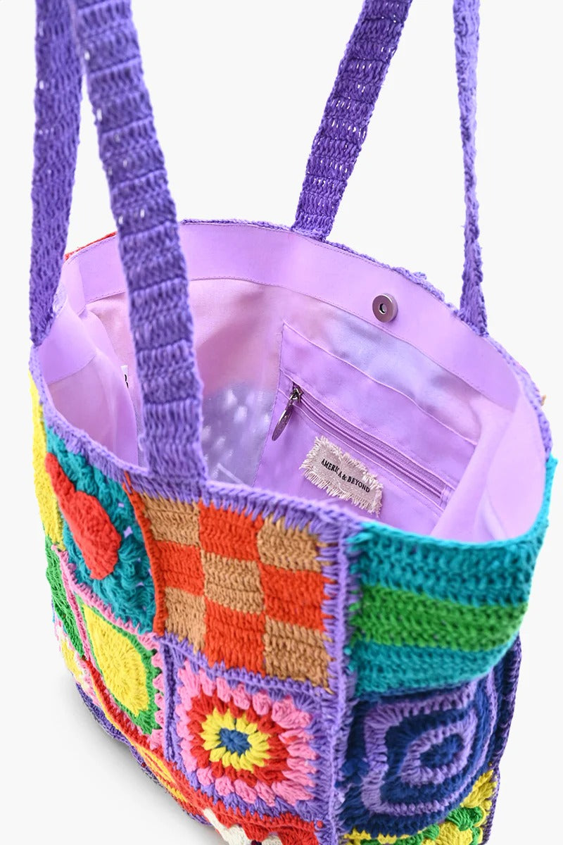 A multicolored crochet tote bag with a playful, patchwork design featuring various geometric and heart-shaped patterns.
