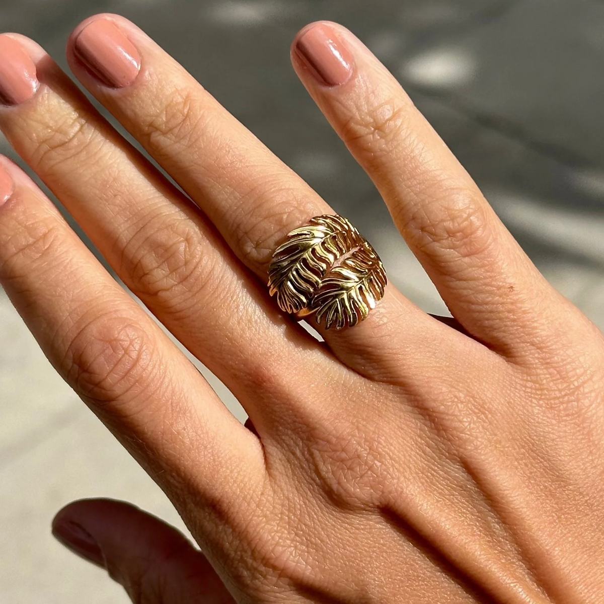 Hand wearing a gold ring with a textured design on a neutral background