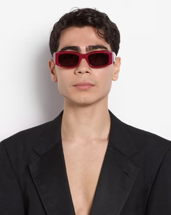 Man wearing red sunglasses and a black suit against a white background