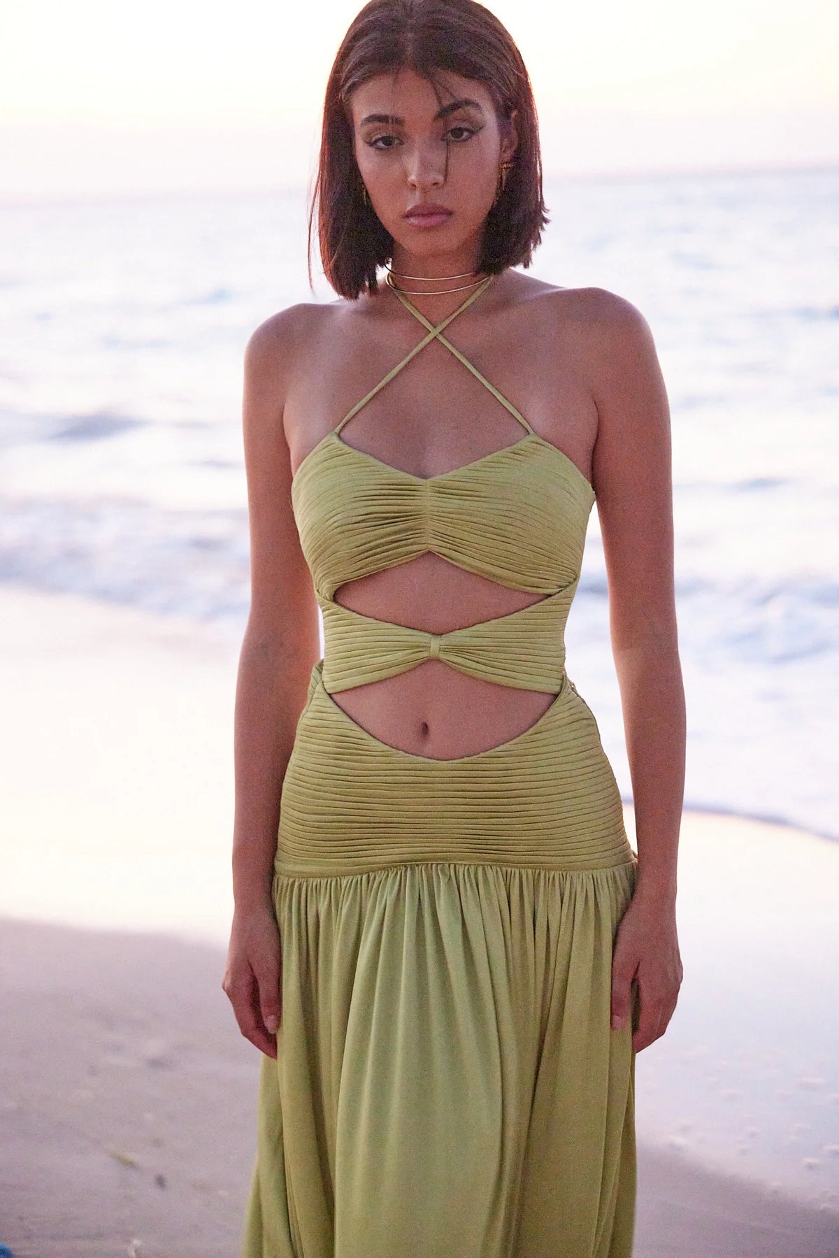 A woman wearing a lime green sleeveless maxi dress with a pleated design standing by the beach.
