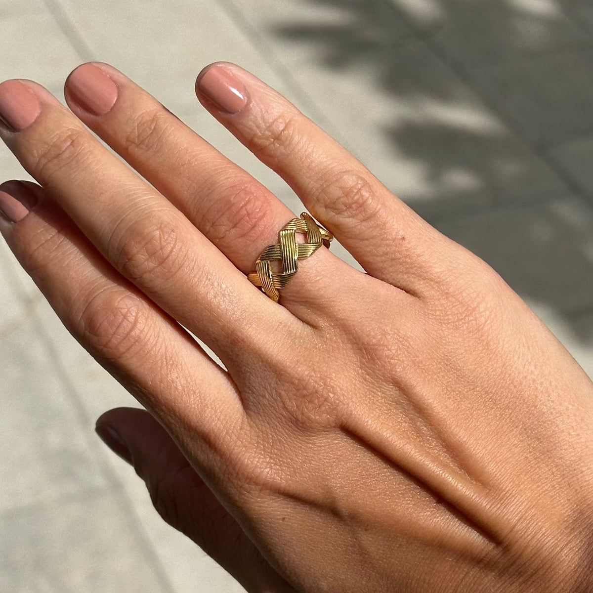 Hand wearing a gold ring with a textured band on a light background
