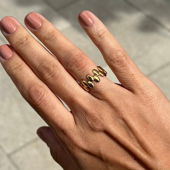 Hand wearing multiple gold rings on a neutral background