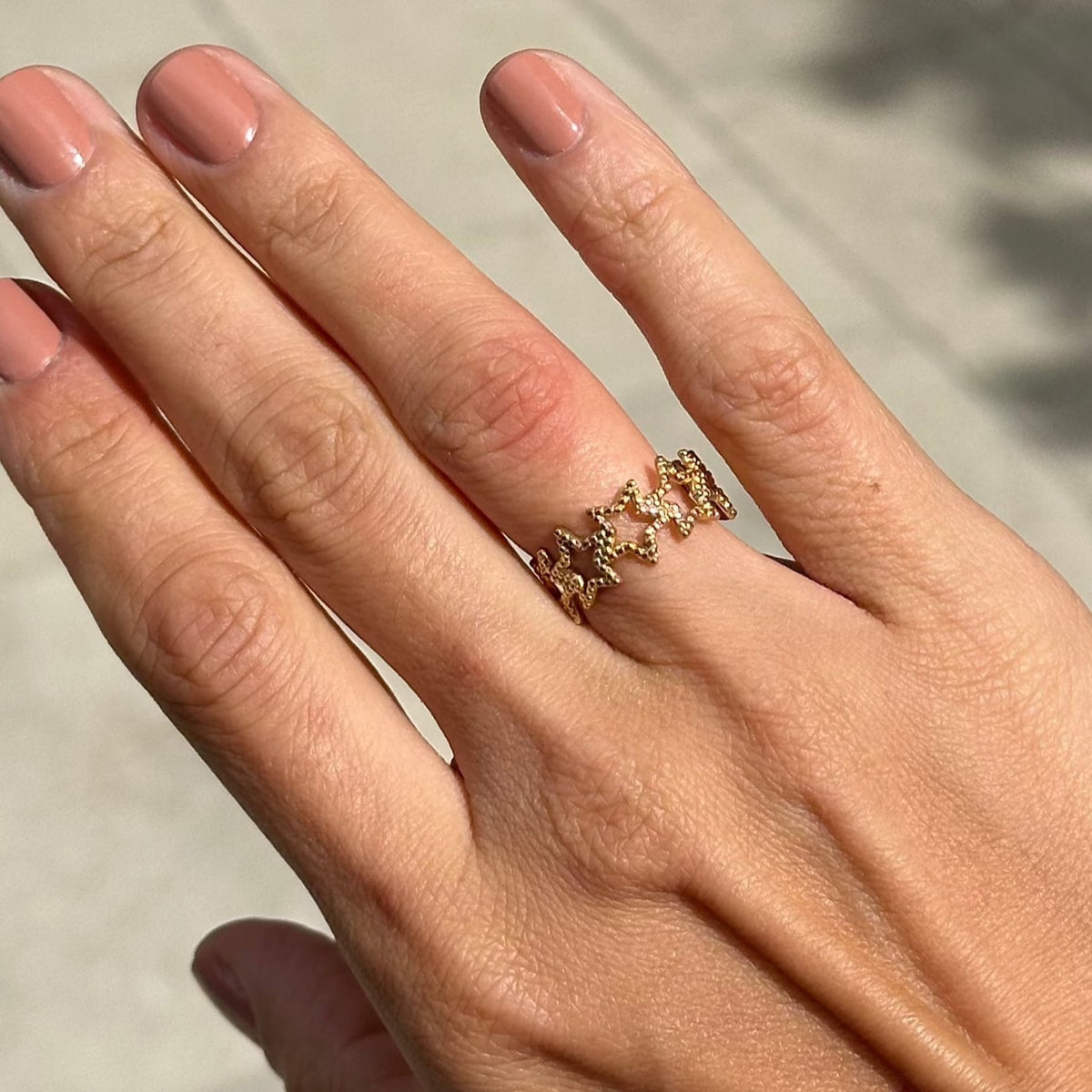 Hand wearing a gold ring with gemstones against a neutral background