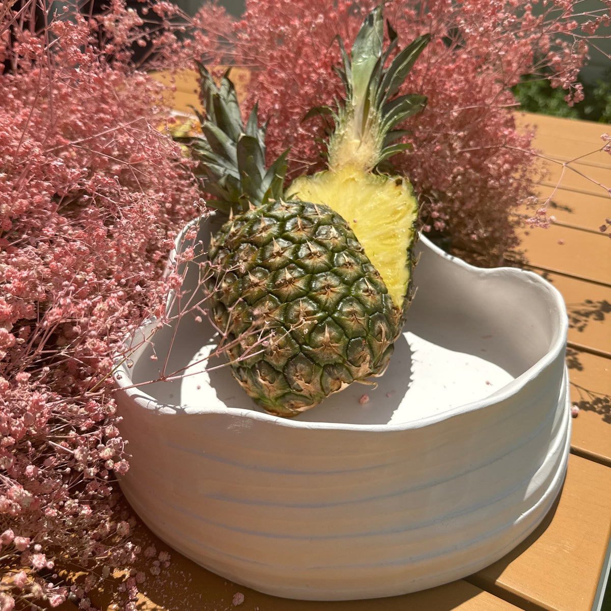 Pineapple in a white bowl with pink flowers in the background