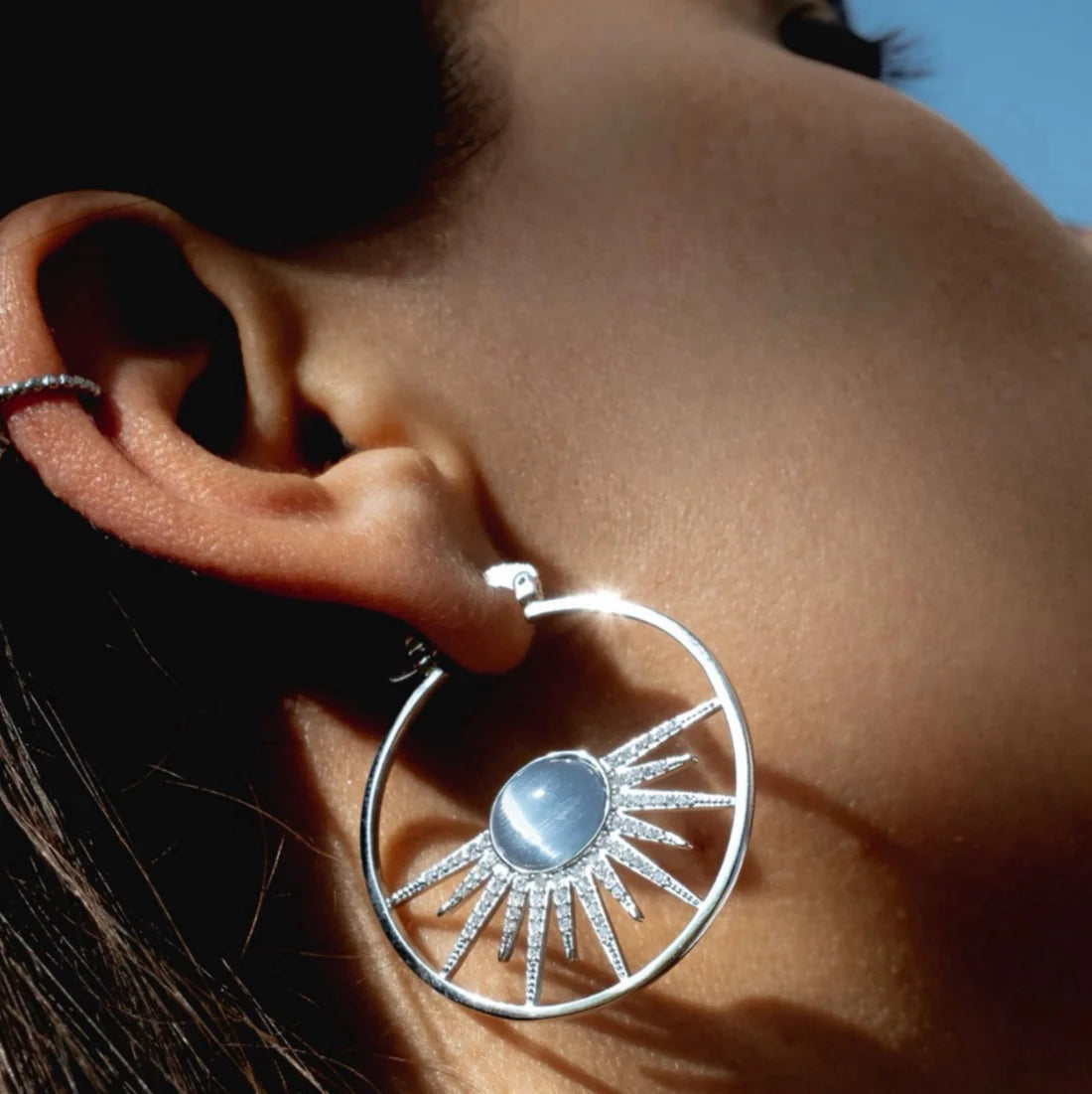 Close-up of a silver earring with a sun design worn by a person.
