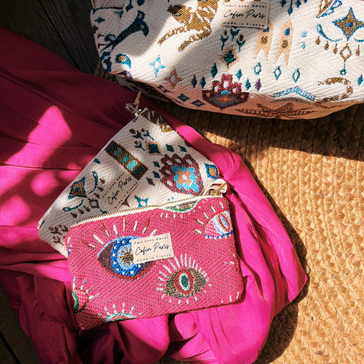 Three embroidered pouches on a textured surface with visible brand labels.