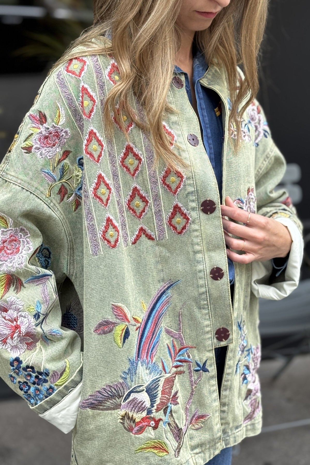 Person wearing a light green embroidered jacket with colorful patterns.