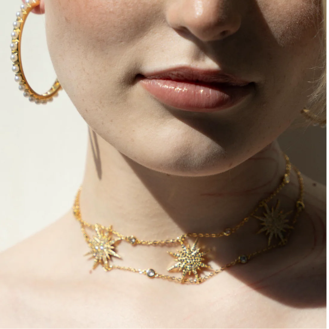 Close-up of a woman wearing gold hoop earrings and necklaces with star designs.