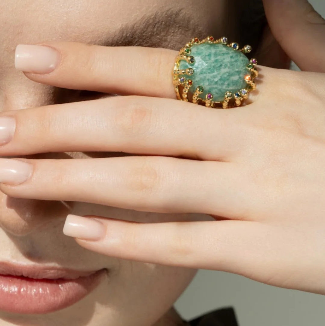 Close-up of a hand wearing a ring with a green gemstone against a neutral background
