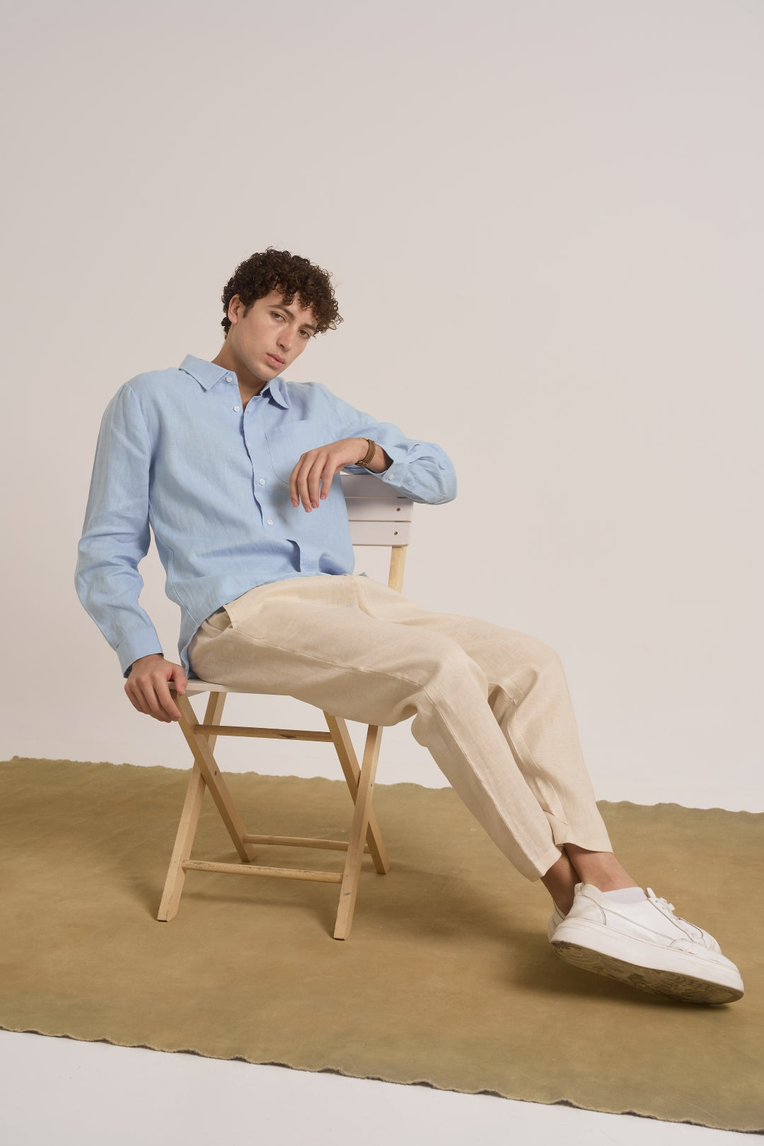 Man sitting on a chair wearing a light blue shirt, beige pants, and white sneakers.