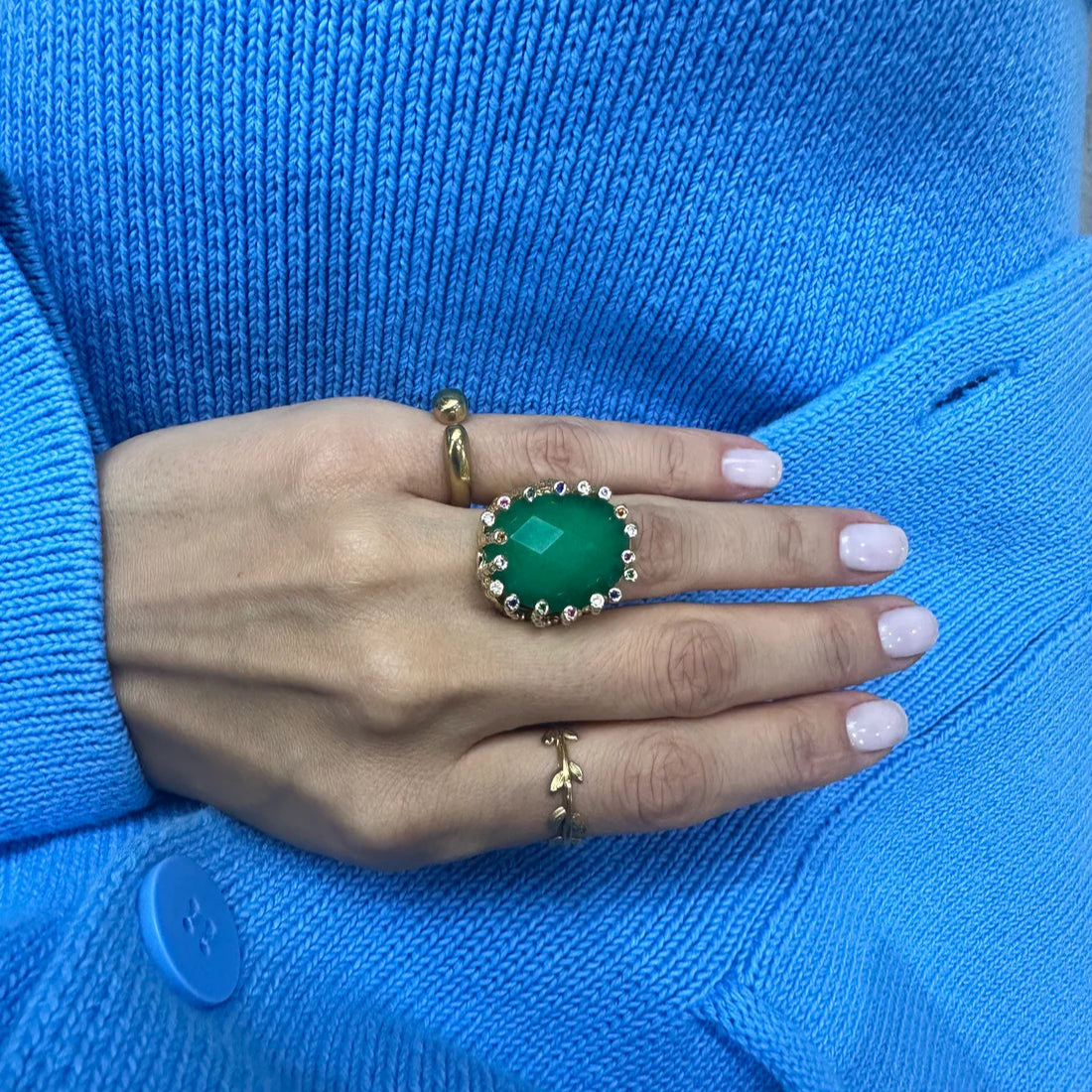 Hand wearing a green ring with a blue sweater background