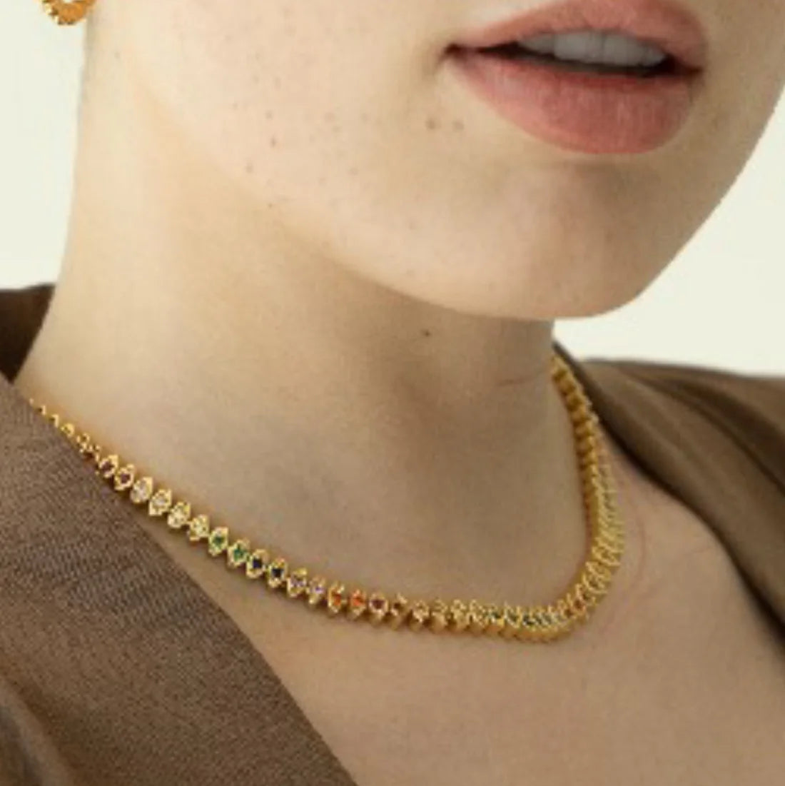 Close-up of a person wearing a gold necklace with a neutral background