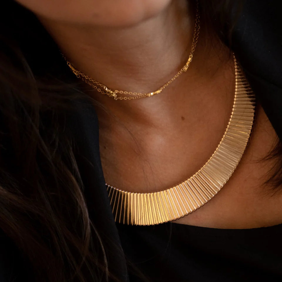 Gold necklace worn by a person against a dark background