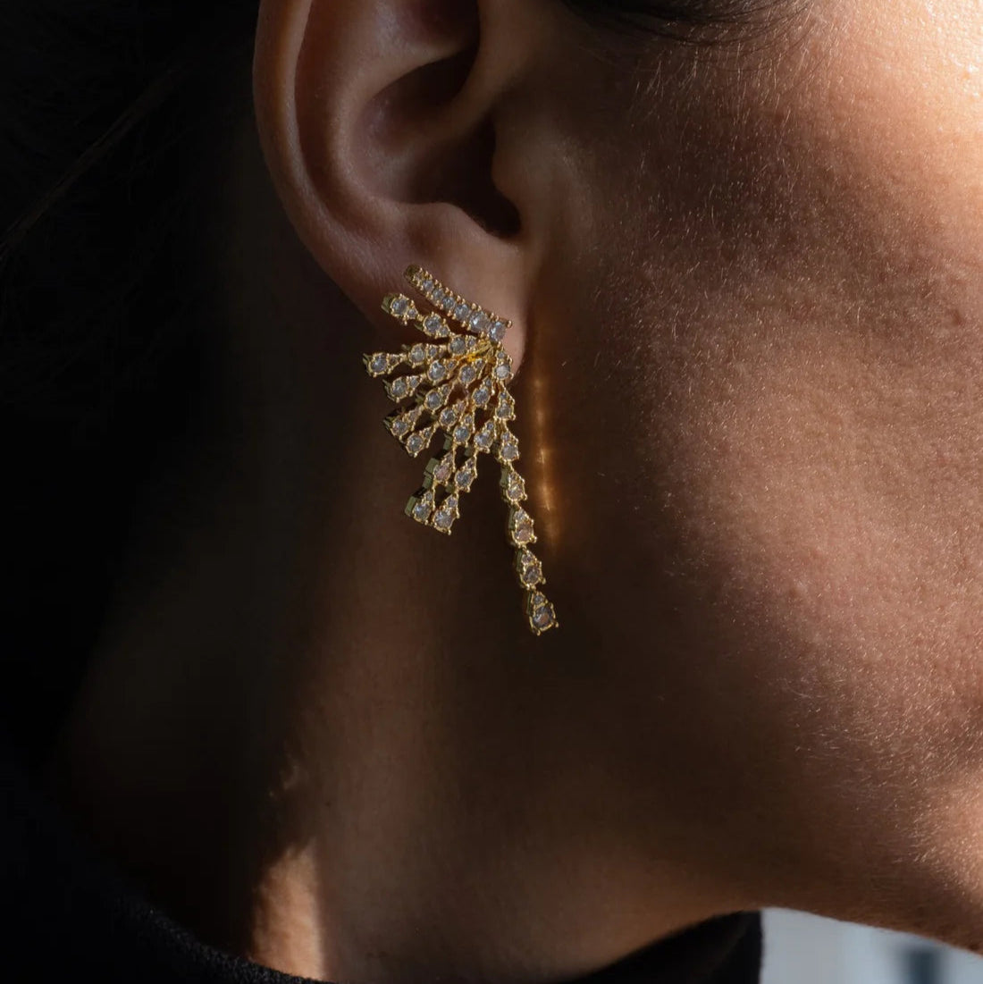 Close-up of a person wearing a sparkling gold earring against a dark background