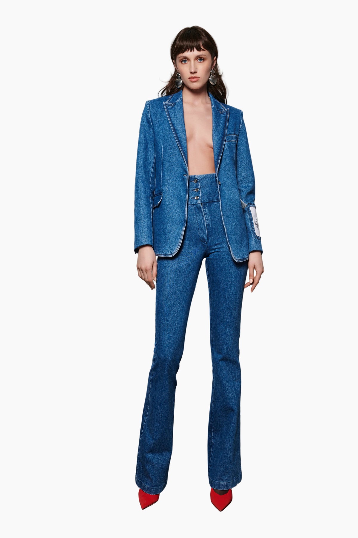 Woman wearing a blue denim suit with red shoes on a plain background