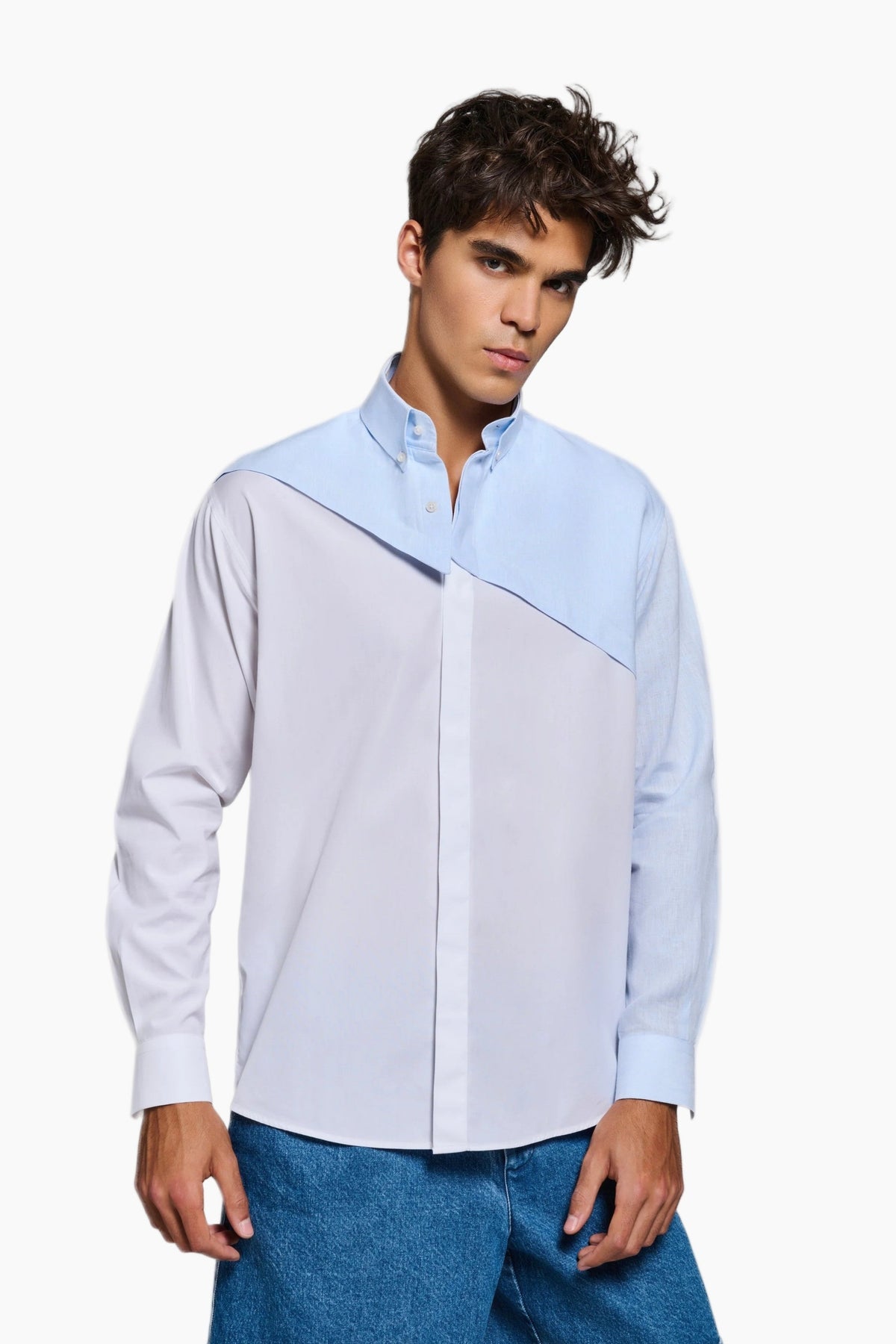 Man wearing a light blue and white color-blocked shirt with blue jeans on a white background