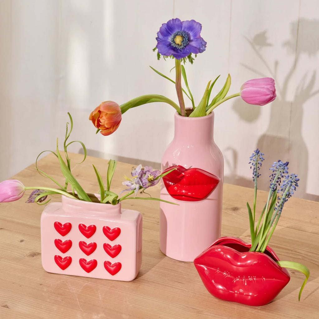 Three decorative vases on a wooden surface with flowers and heart designs.
