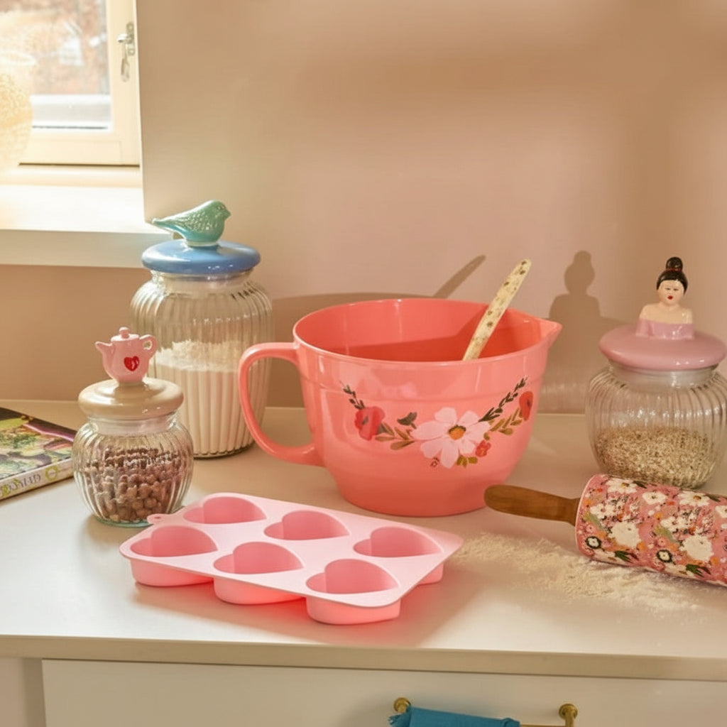 Pink kitchen items including a mixing bowl, baking tray, and rolling pin on a countertop.