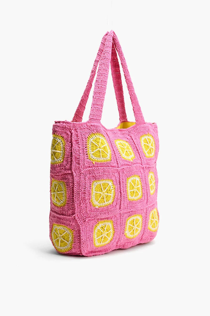 A vibrant pink and yellow crochet beach tote with metallic button closure and double shoulder straps.
